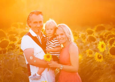 Lachende Familie mit kleinem Jungen vor einem Sonnenblumenfeld im Sonnenuntergang